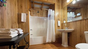 A wooden-floored bathroom with a bathtub, a sink, a toilet, and a mirror. - Vaulted-Ceiling Cabin for 4 with King Bed + Bunks, Full Kitchen & Pond Views (Zwolle)