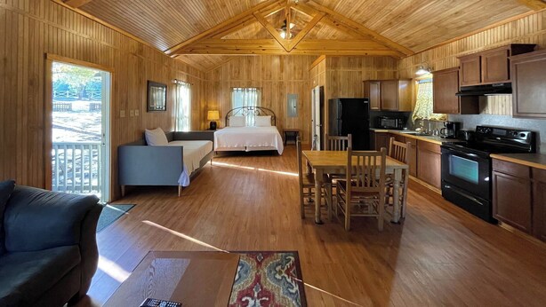 A wooden cabin interior with a bedroom, living area, and kitchen. - Vaulted-Ceiling Cabin for 4 with King Bed + Bunks, Full Kitchen & Pond Views (Zwolle)