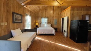 A wooden cabin with two beds, a dining table, a refrigerator, and a framed picture on the wall. - Vaulted-Ceiling Cabin for 4 with King Bed + Bunks, Full Kitchen & Pond Views (Zwolle)