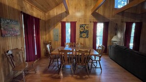 A wooden interior with a dining table, chairs, a sofa, and a painting on the wall. - Spacious 1-Bedroom Cabin with Full Kitchen, Vaulted Ceiling & Outdoor Space (Zwolle)