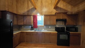 A kitchen with wooden cabinets, a refrigerator, a stove, and a microwave. - Spacious 1-Bedroom Cabin with Full Kitchen, Vaulted Ceiling & Outdoor Space (Zwolle)