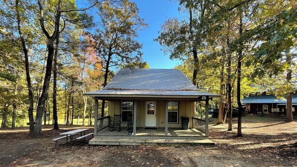 A small, single-story building with a porch, surrounded by trees. - Spacious 1-Bedroom Cabin with Full Kitchen, Vaulted Ceiling & Outdoor Space (Zwolle)