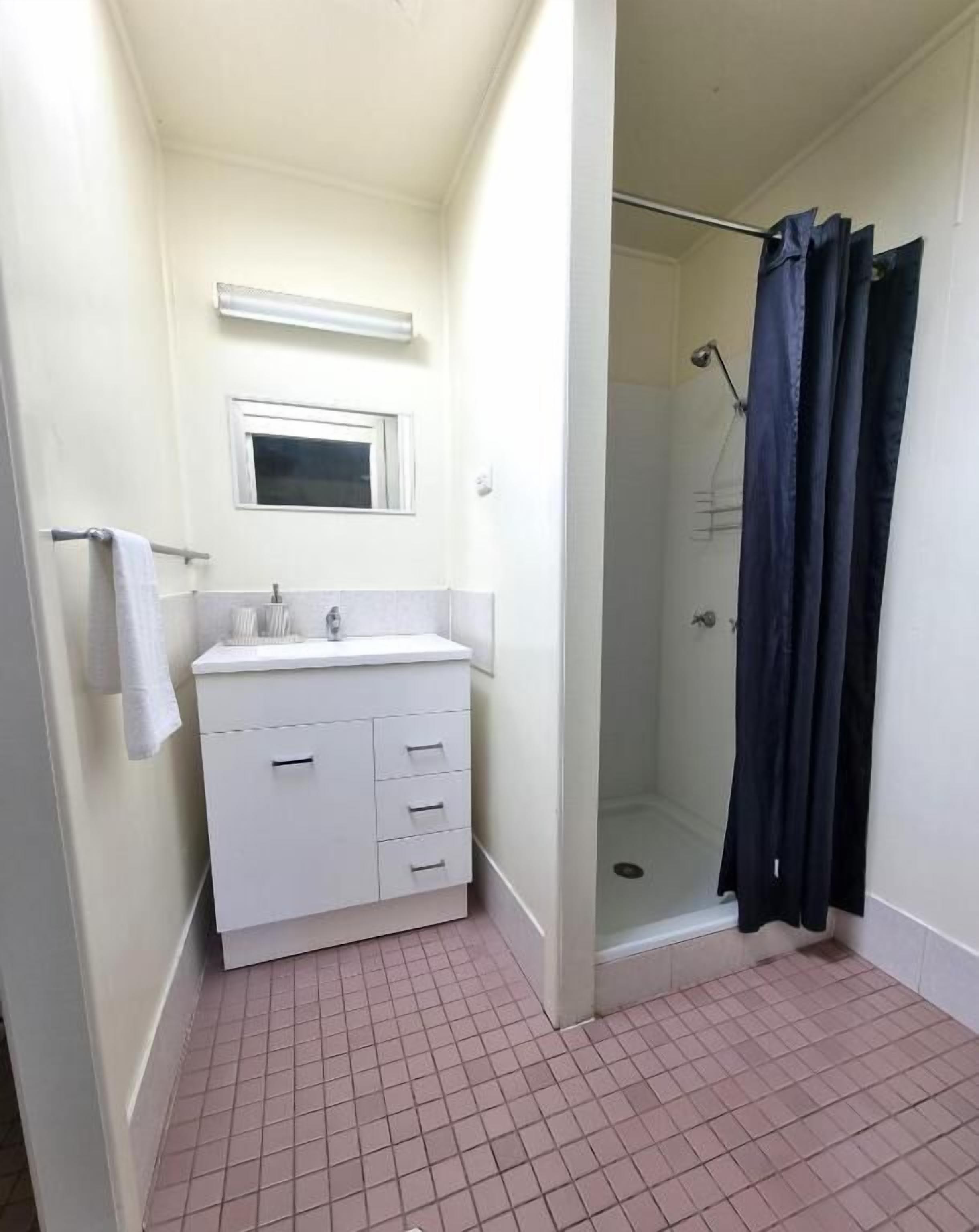 Un baño pequeño con lavamanos blanco, espejo y ducha con cortina oscura.