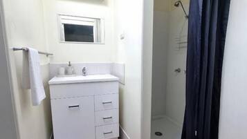 Un baño pequeño con lavamanos blanco, espejo y ducha con cortina oscura.