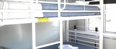 Habitación con literas, ventana, radiador y una puerta blanca.