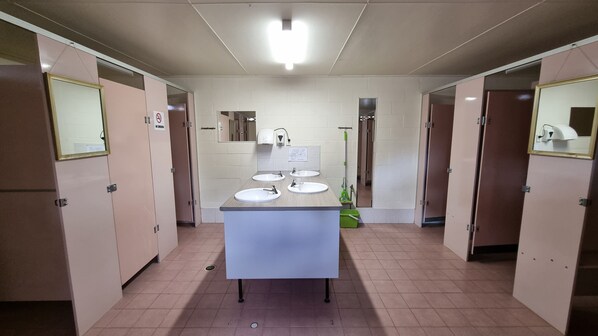 A public restroom with three sinks, a mirror, a mop, and a trash bin. - Country Style Holiday Park (Glen Aplin)