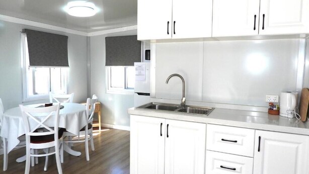 A modern kitchen with white cabinets, a stainless steel sink, and a dining area with a table and chairs. - Country Style Holiday Park (Glen Aplin)