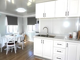 A modern kitchen with white cabinets, a stainless steel sink, and a dining area with a table and chairs.