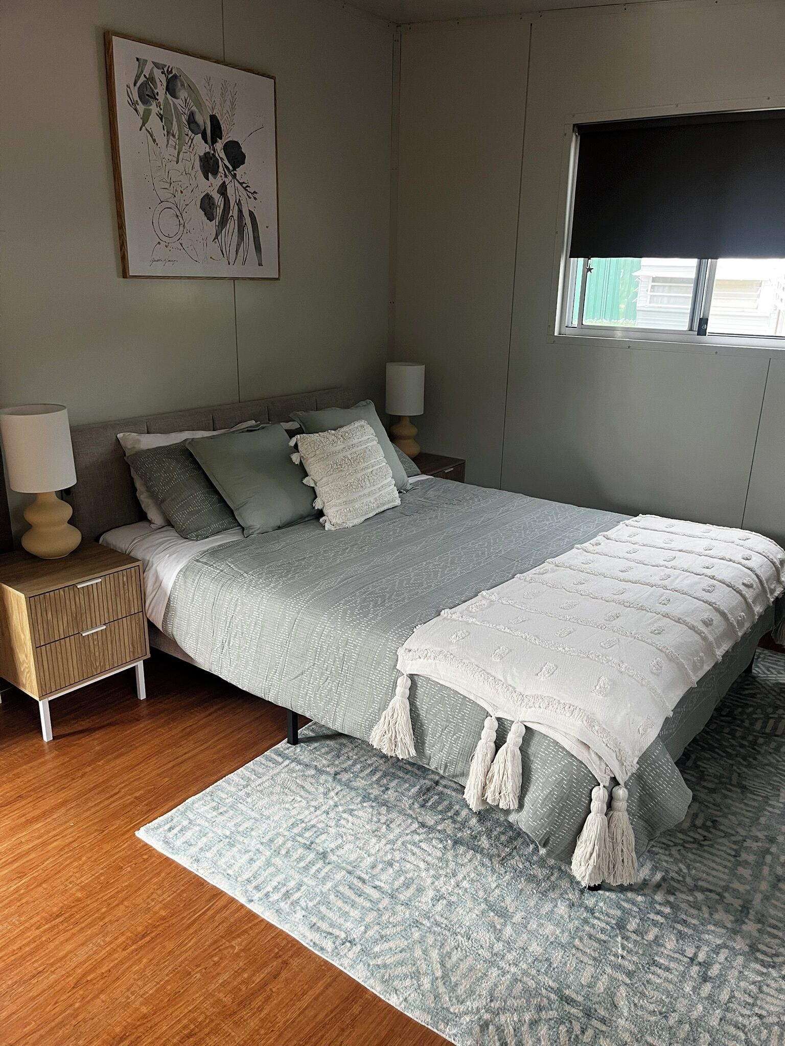 A bedroom with a bed, nightstands, a lamp, a window, and a painting on the wall.
