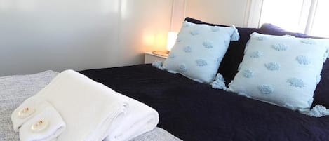 A neatly made bed with a dark blue bedspread and two pillows with a light blue floral pattern. There are folded white towels on the bed.