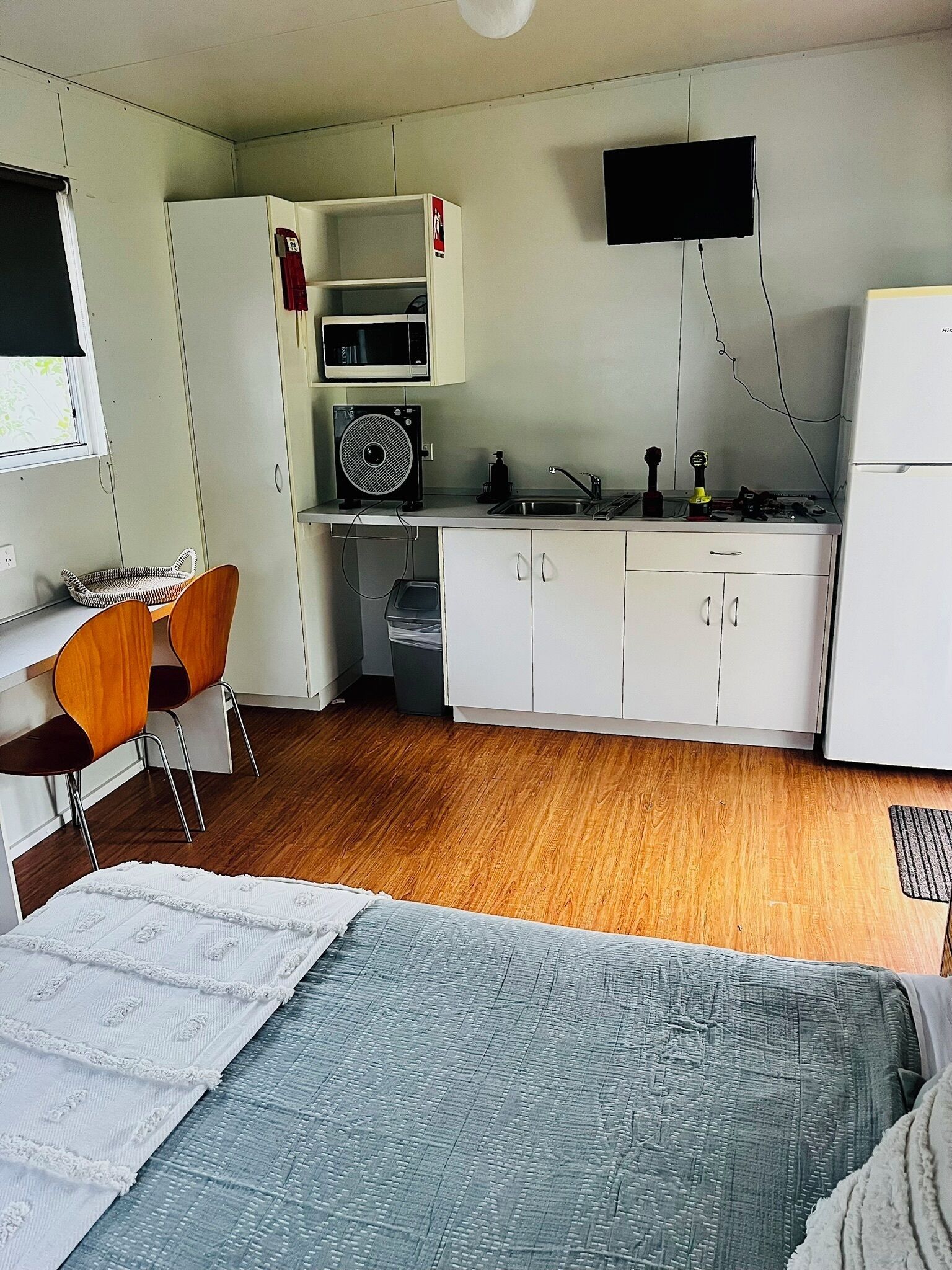A compact hotel room with a bed, a kitchenette, a small dining area, and a single chair.