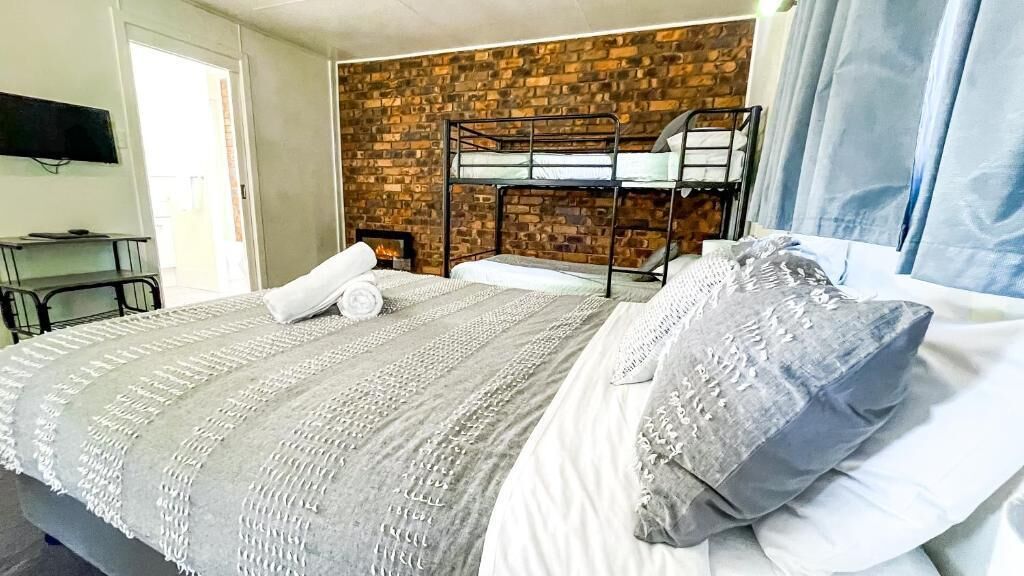 A bunk bed room with a brick wall, a flat-screen TV, and a window with curtains.