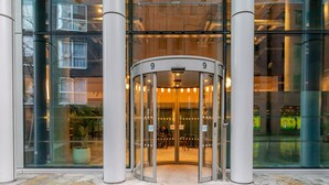 Una puerta giratoria con el número 9, amplios ventanales de vidrio y una fachada de edificio moderna.
