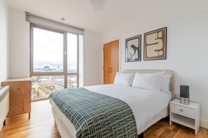 A modern bedroom with a large window, a bed with a patterned blanket, a nightstand, and two abstract wall art pieces. - Blueground | Shadwell, balcony, nr Tower Bridge (London)