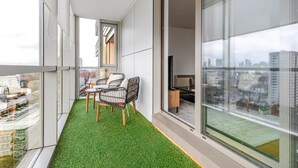 Een balkon met kunstgras, twee stoelen en een televisie op de achtergrond.
