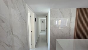 A modern hallway with marble walls and a glossy white floor, leading to a bathroom with a large mirror and a wooden panel. - Copacabana 4 bedrooms (2 suites) with side sea and mountain views (Rio de Janeiro)