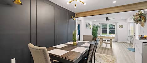 A modern dining area with a dark wood table, beige chairs, and a chandelier.