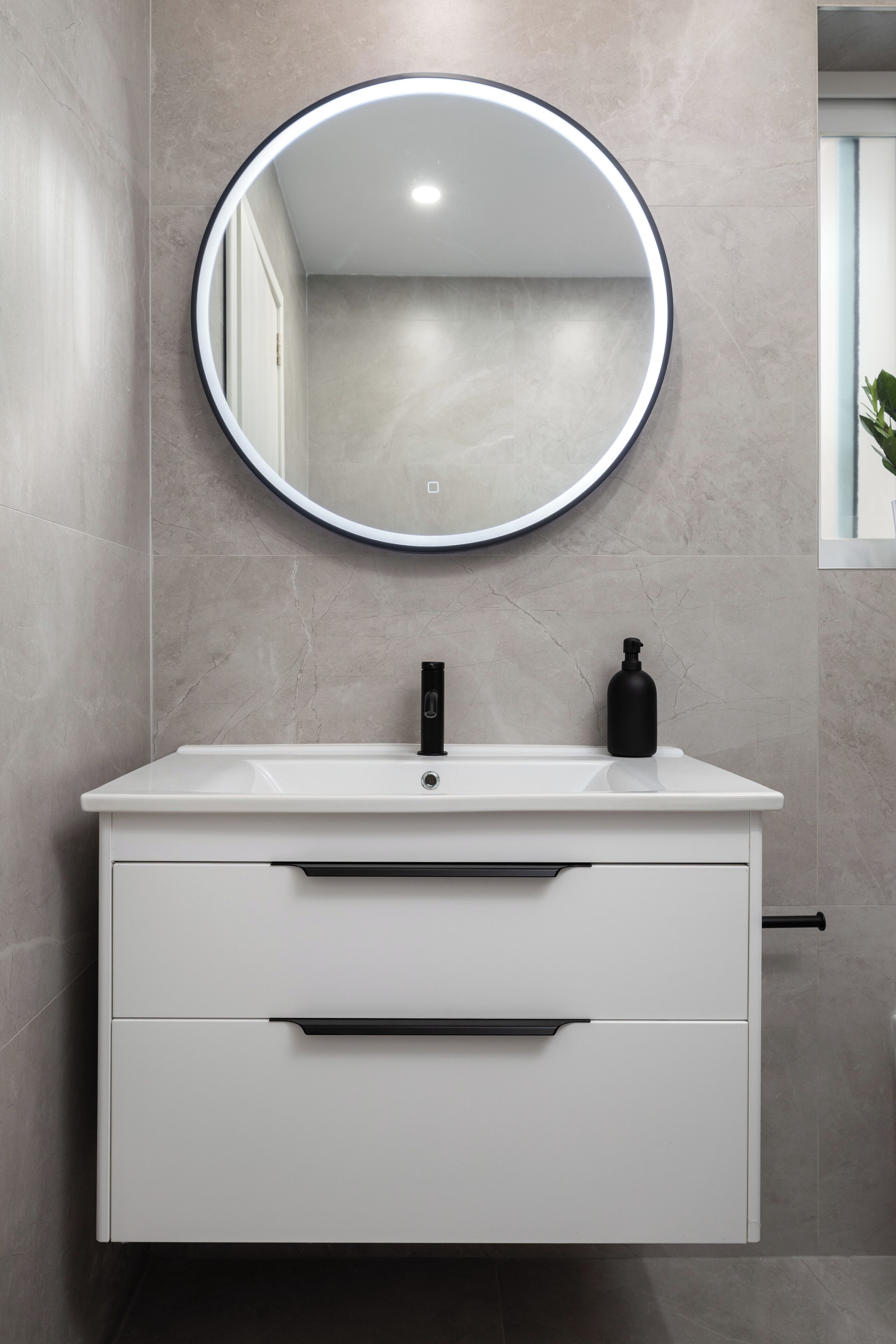 A bathroom with a white vanity, a round mirror, and a black soap dispenser.