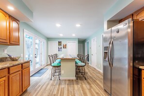 A kitchen with wooden cabinets, a stainless steel refrigerator, and a dining table with chairs. - Luxury Pocono Retreat• 3 King Beds•Hot Tub, Game Room, Fireplace & Firepit (East Stroudsburg)