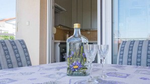 A glass bottle with a floral design on a table with a patterned tablecloth, accompanied by two wine glasses. - Holiday apartment with balcony (Biograd na Moru)