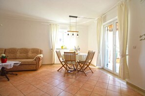 A living room with a sofa, a dining table with chairs, a small table with a lace tablecloth, and a hanging light fixture. - Holiday apartment with air conditioning (Pula)