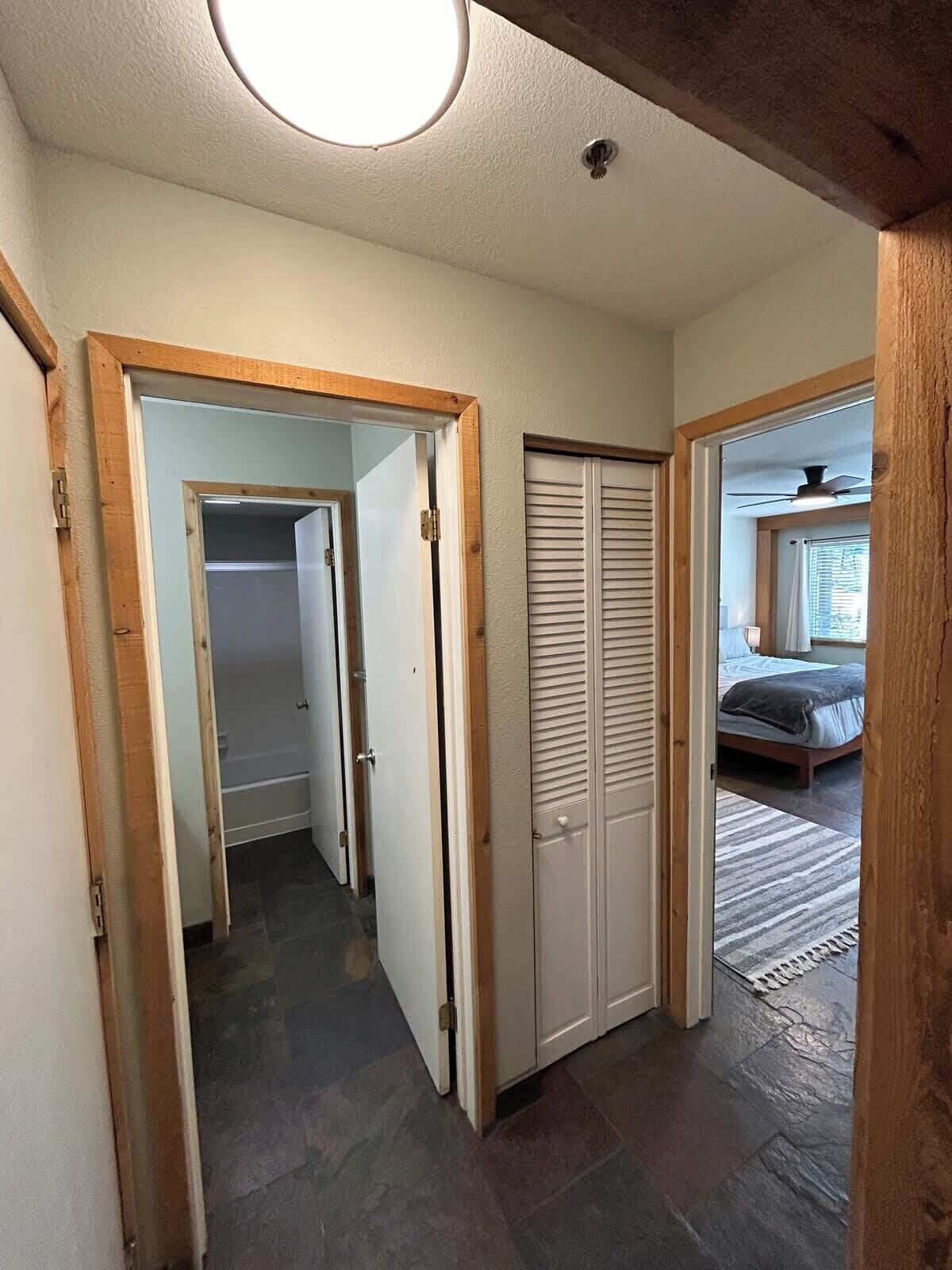 Un pasillo con un marco de puerta de madera, un armario con puertas persianas y un dormitorio con cama y ventana.