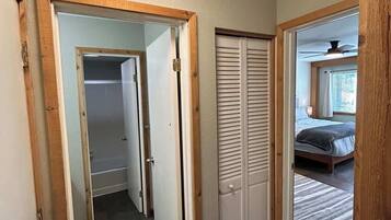 Un pasillo con un marco de puerta de madera, un armario con puertas persianas y un dormitorio con cama y ventana.