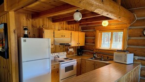 A wooden cabin kitchen with a refrigerator, stove, microwave, and wooden cabinets. - Wilderness, wildlife, and fishing cabin - The Ponderosa at Alta Ranch (Darby)