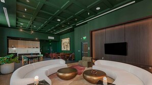A modern lobby with curved white sofas, a dining area, and a flat-screen TV mounted on a wooden panel. - Crosby 31 | Signature Skyline Residence (Miami)