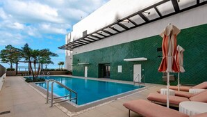 A swimming pool with a metal ladder, lounge chairs, and a covered area with umbrellas. - Crosby 31 | Signature Skyline Residence (Miami)