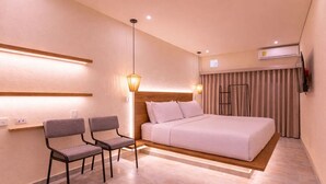 Una habitación de hotel moderna con una cama, dos sillas, una mesita de noche, una lámpara y un equipo de aire acondicionado.