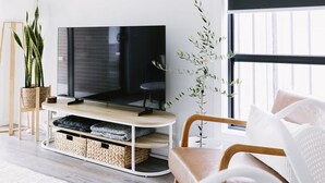 Un salon moderne avec un téléviseur à écran plat posé sur un meuble en bois, des paniers en osier placés sous le meuble, une chaise en bois et une plante en pot.