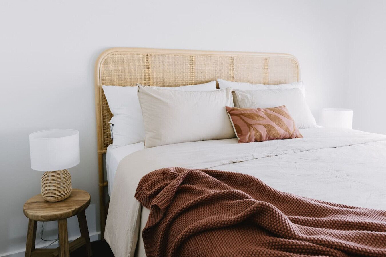 Un lit bien fait, avec une couette blanche, un plaid marron en tricot et plusieurs coussins.