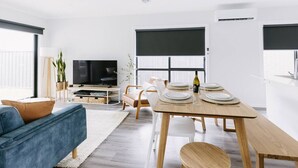 Un salon moderne avec un canapé, une table à manger pour quatre personnes et un téléviseur.