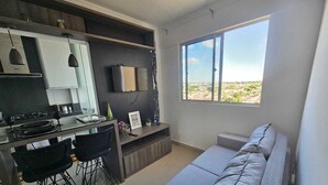 Uma sala de estar moderna com um sofá cinzento, uma área de refeições com uma mesa de vidro e cadeiras pretas, uma janela grande com vista para o deserto e uma TV de tela plana montada na parede.