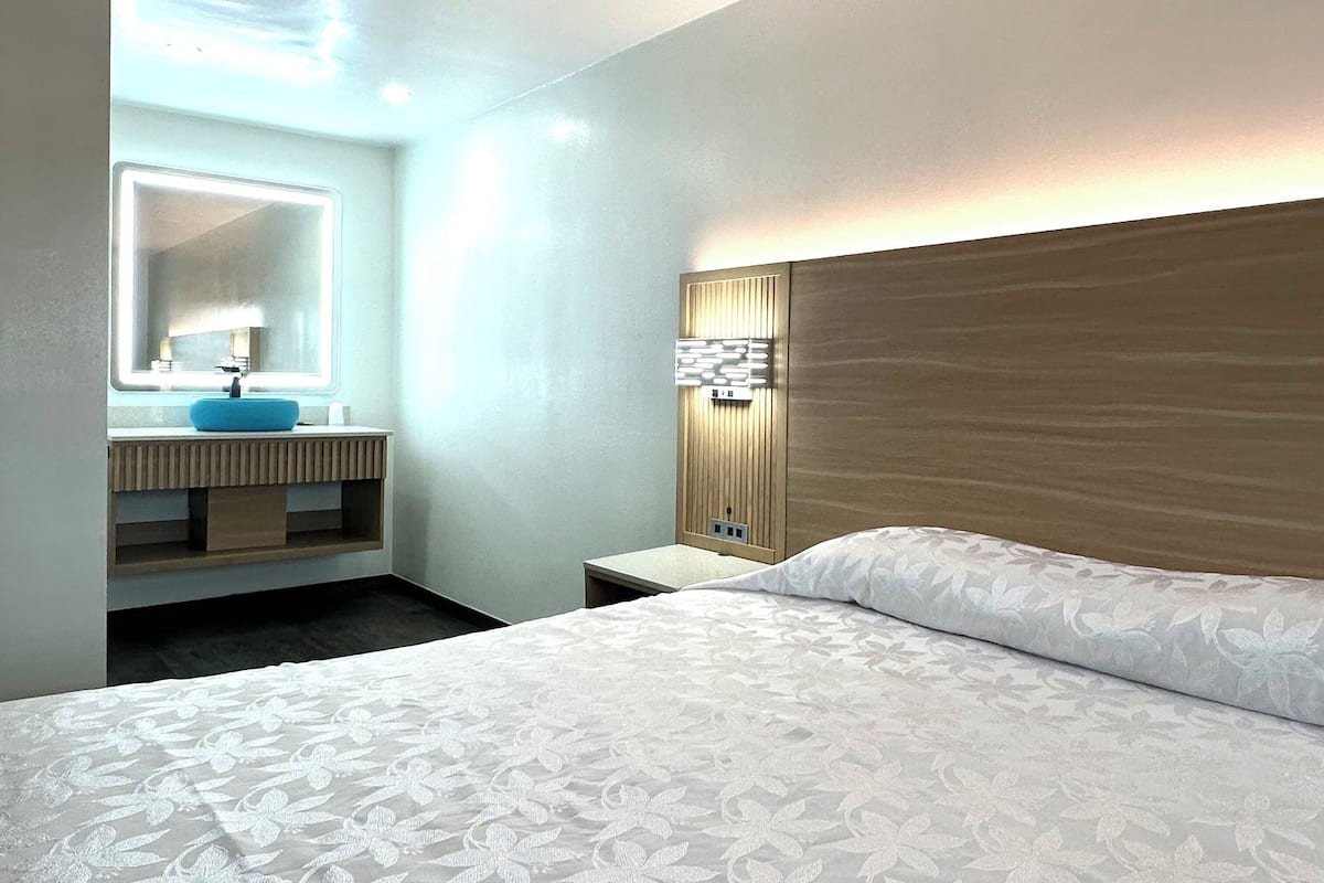 A hotel room with a large bed, a bedside table, a mirror, and a bathroom with a sink and vanity.