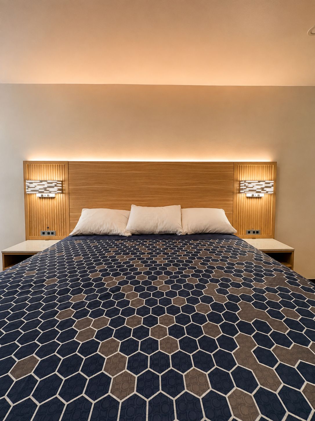 Habitación de hotel con una cama grande, cabecero de madera, dos mesitas de noche e iluminación empotrada.