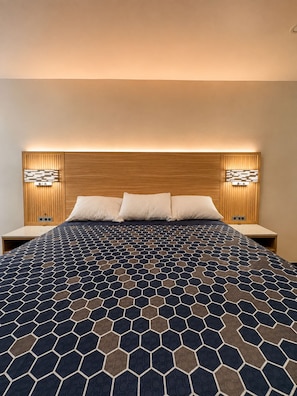 A hotel room with a large bed, wooden headboard, two bedside tables, and wall-mounted lighting. - Nubell Motel (Bell Gardens)
