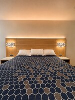Habitación de hotel con una cama grande, cabecero de madera, dos mesitas de noche e iluminación empotrada.