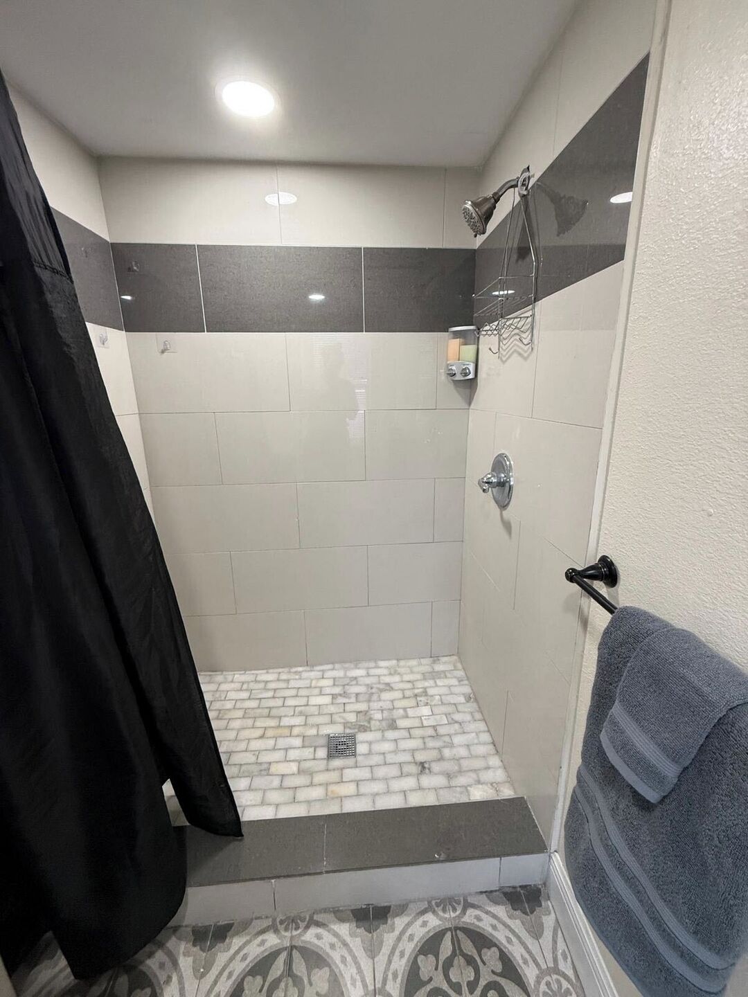 Un espace douche avec un sol carrelé, une pomme de douche et un porte-serviettes.