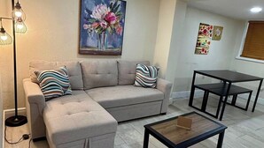Un salón con sofá, reposapiés, mesa de centro y un cuadro en la pared.