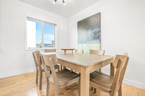 Uma área de refeições com mesa e cadeiras de madeira, uma janela com vista e um quadro abstrato grande na parede.