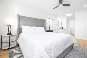 Quarto moderno com uma cama grande, um ventilador de teto e um banheiro visível ao fundo.