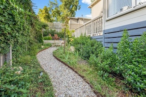 Ein Gartenweg führt zu einem Haus mit einer Holzterrasse und einem Stuhl.