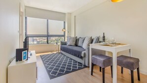 Un salon moderne avec un canapé, une petite table à manger, une table basse et une vue dégagée sur l’extérieur grâce à une grande fenêtre.
