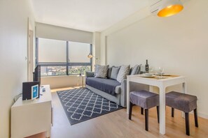 Ein modernes Wohnzimmer mit einer Couch, einem kleinen Esstisch, einem Couchtisch und Blick durch ein großes Fenster.