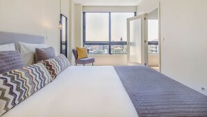 Une chambre avec un grand lit, une chaise et une vue sur la ville par une grande fenêtre.