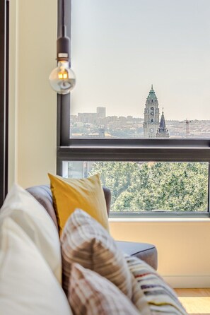 Ein Zimmer mit einem Bett, einem Fenster mit Blick auf eine Stadtlandschaft und einen Glockenturm, sowie einer hängenden Leuchte.