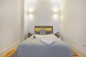 Ein schmales Hotelzimmer mit einem Bett, zwei Nachttischen, einer Ablagefläche und Wandleuchten.