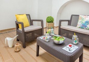 Ein Rattansitzmöbel-Set mit Kissen, ein kleiner Tisch mit einer Salatschüssel, einer Karaffe und einer Zierpflanze.